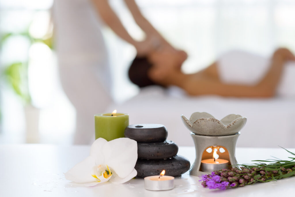 spa stones and candles with a blurred background of client receiving a massage treatment