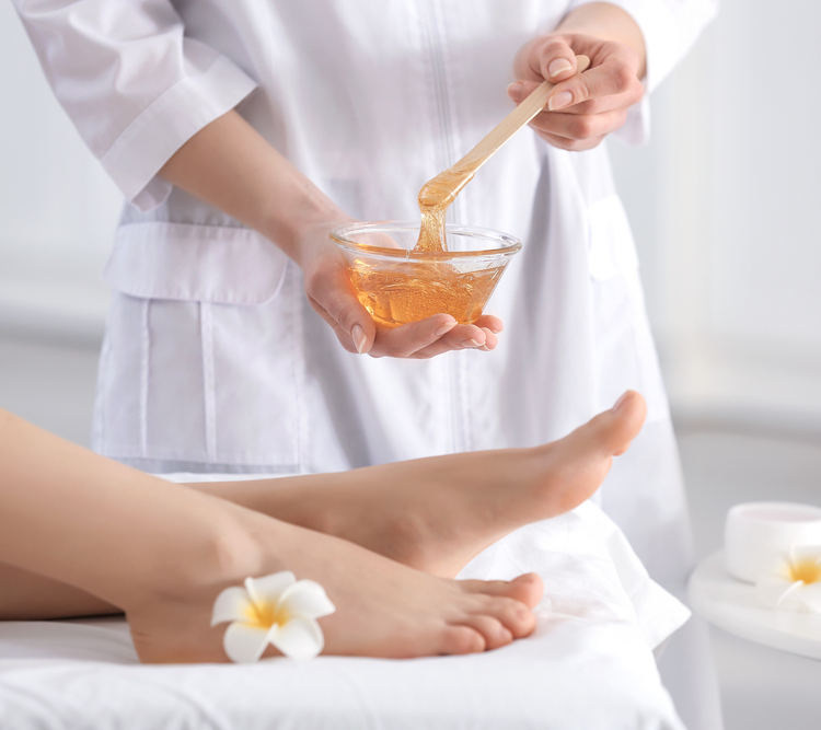 Beautician waxing female legs in spa center